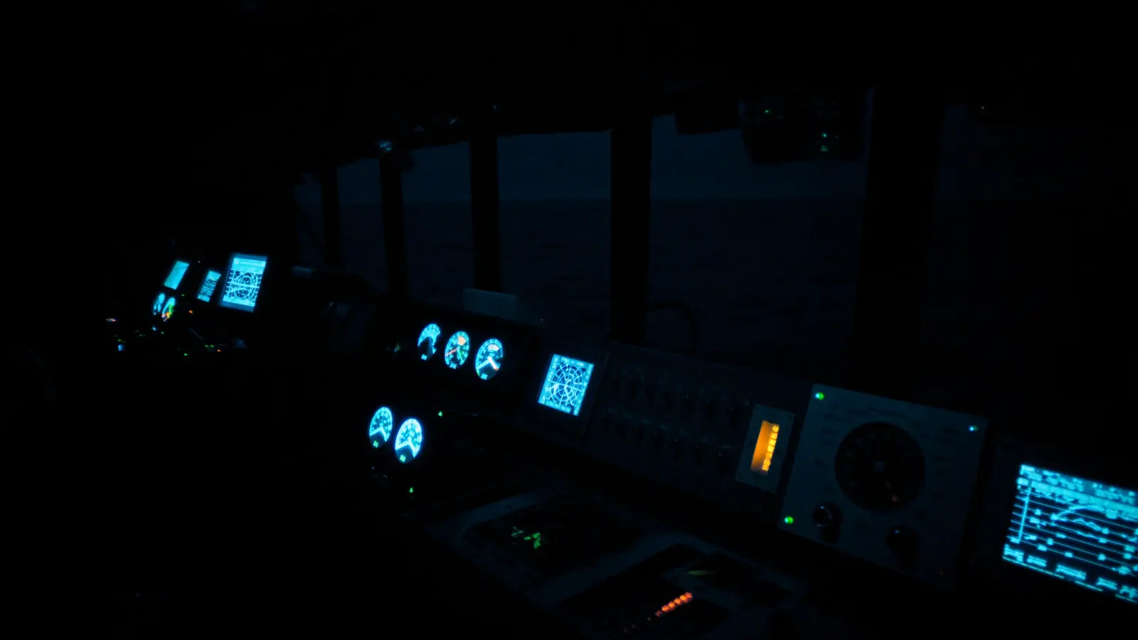 A ship's wheelhouse at night, instrument screens carrying the only light in the room.
