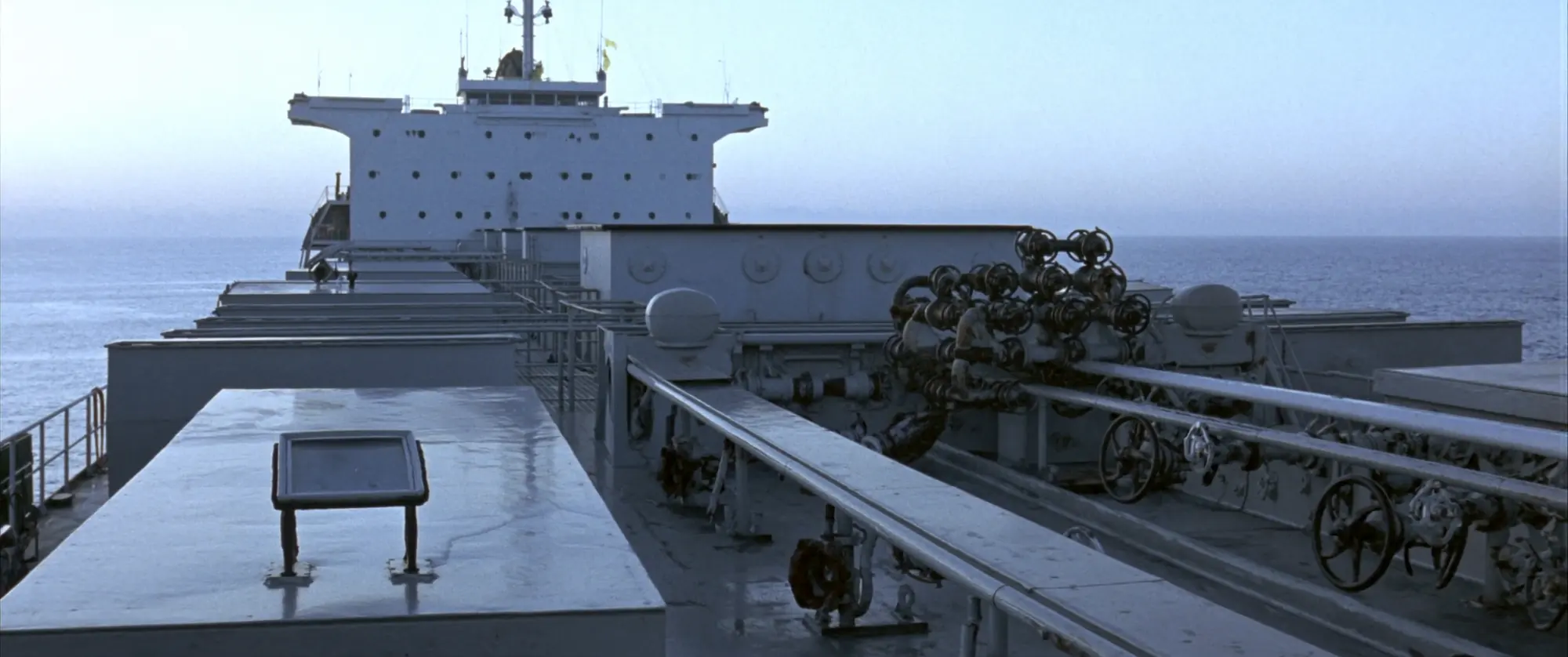 The main deck of a product tanker, manifold and pipework running forward under an overcast sky.