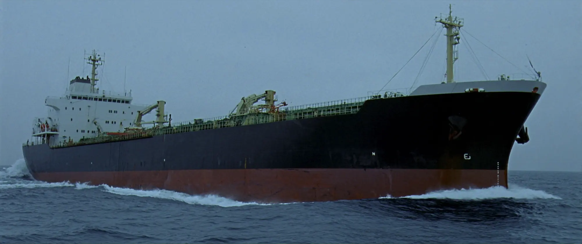 A laden product tanker under way in a grey open sea.